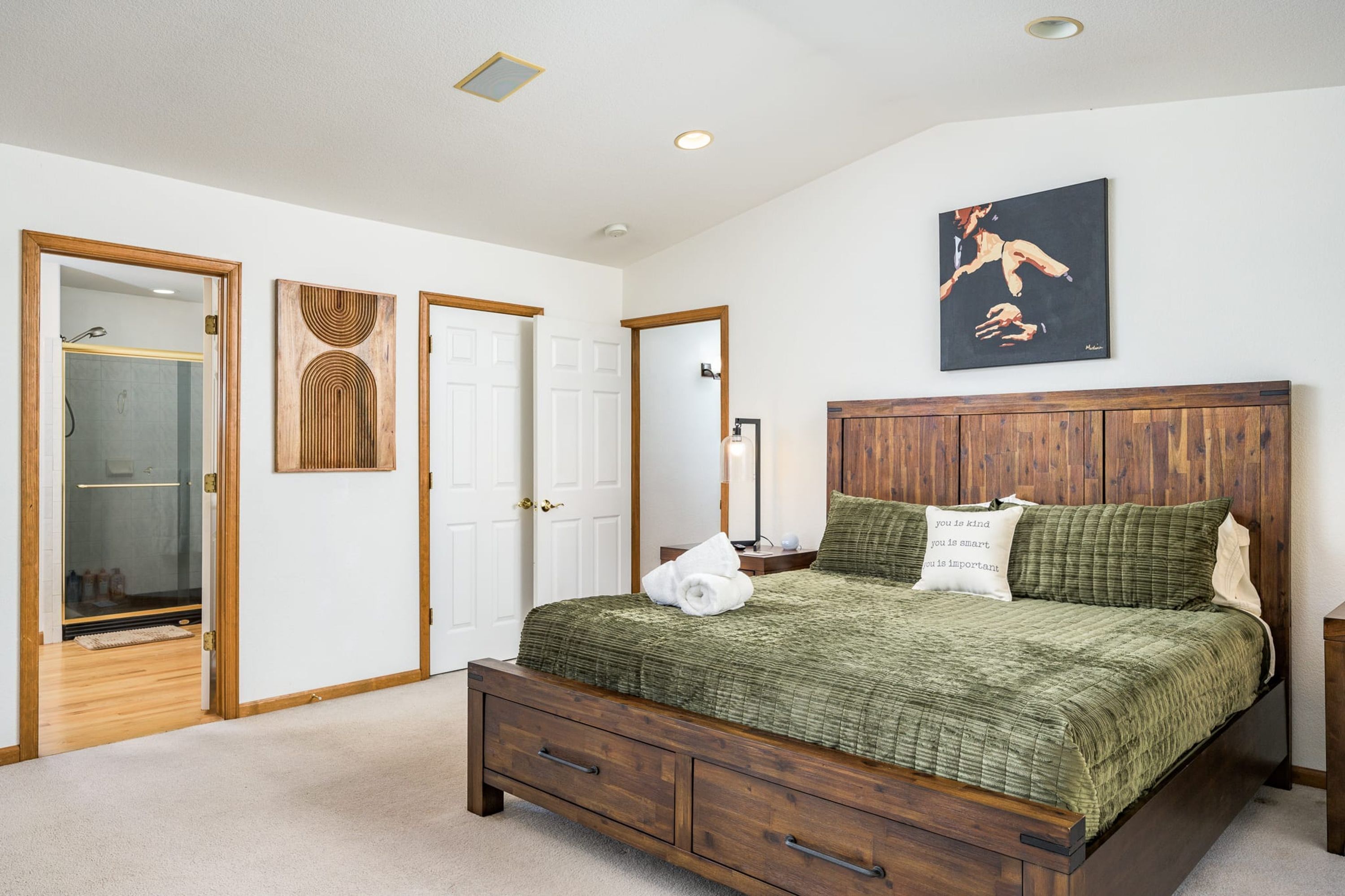 Une chambre à coucher avec un lit, une table de chevet, une commode, un tableau et une porte avec un miroir.