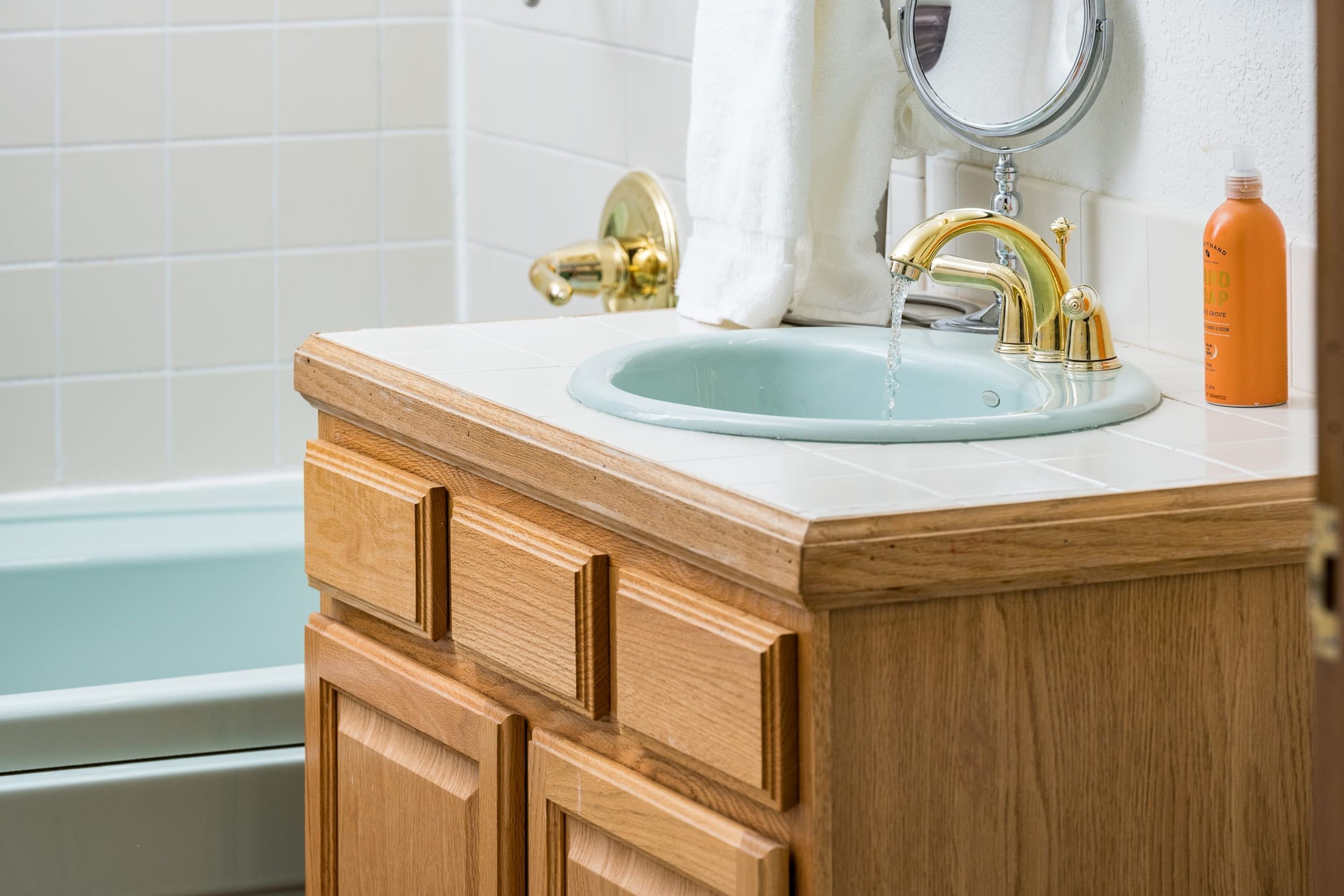 Une salle de bain avec un meuble-lavabo en bois, un évier avec un robinet doré et une baignoire blanche.