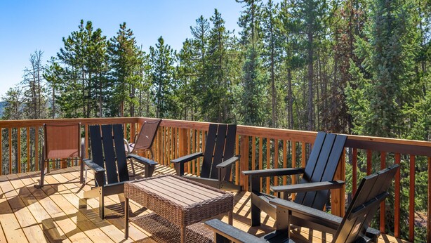 Una terraza de madera con mobiliario exterior, rodeada por un bosque.