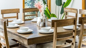 Una mesa de comedor de madera con platos y tazones blancos, rodeada de sillas de madera.