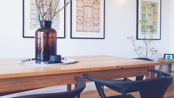 A wooden dining table with a vase of branches, framed menus on the wall, and black chairs.