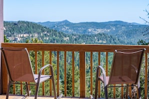 A balcony with two chairs facing a scenic view of a forested mountain range.