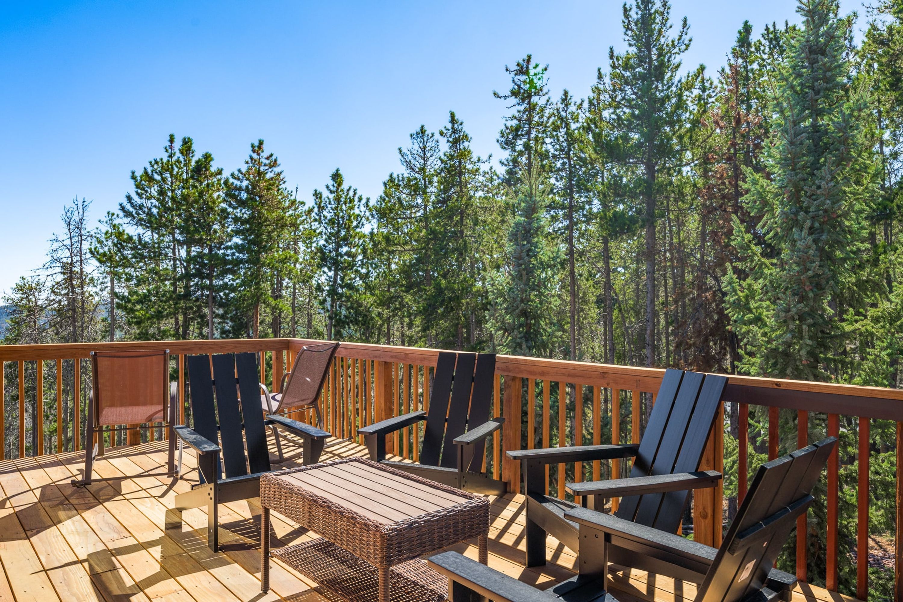 A wooden deck with outdoor furniture, surrounded by a forest.