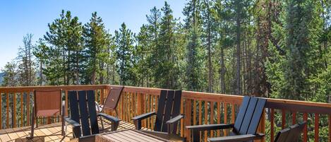 A wooden deck with outdoor furniture, surrounded by a forest.