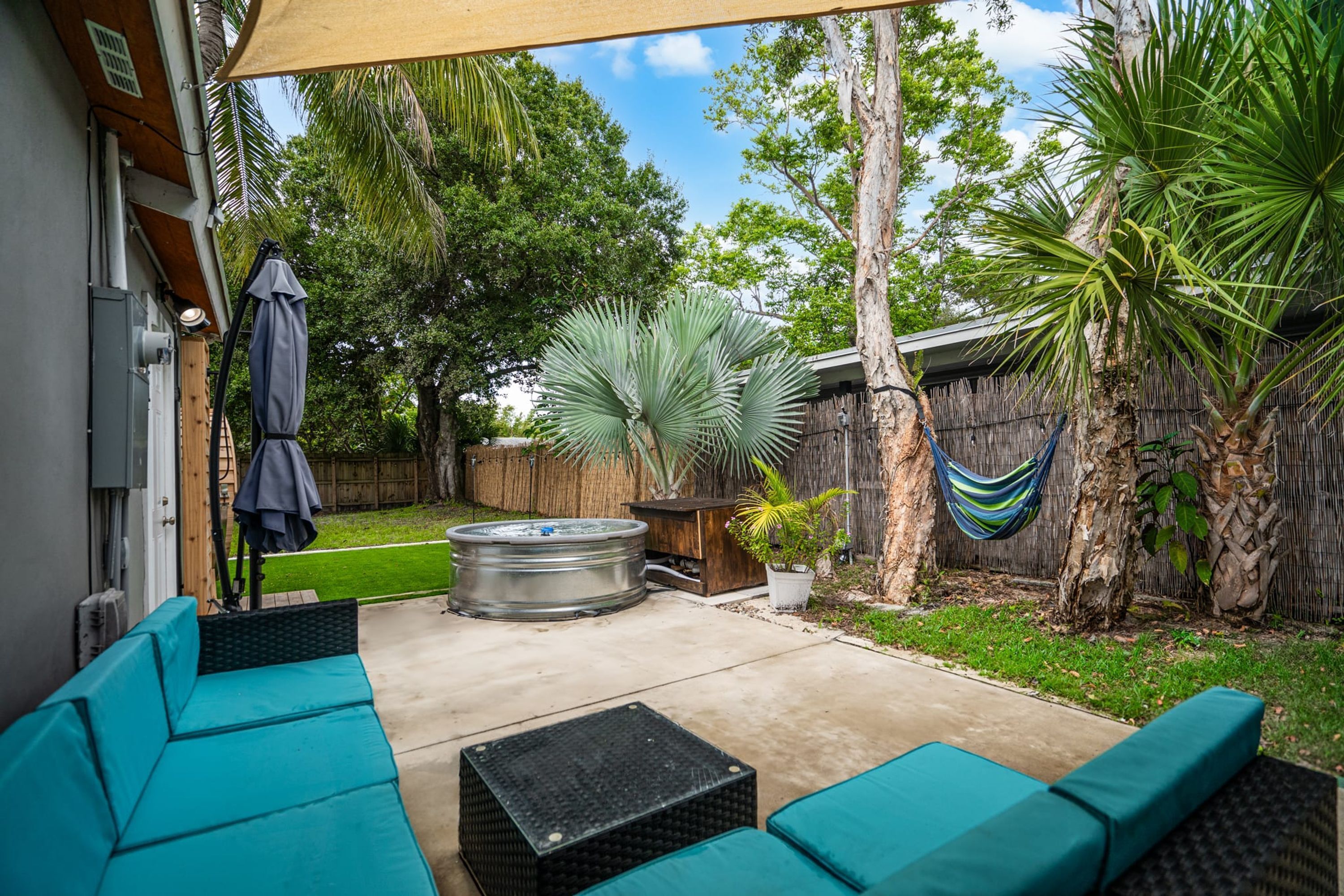 A patio with teal cushioned seating, a hot tub, and a hammock.