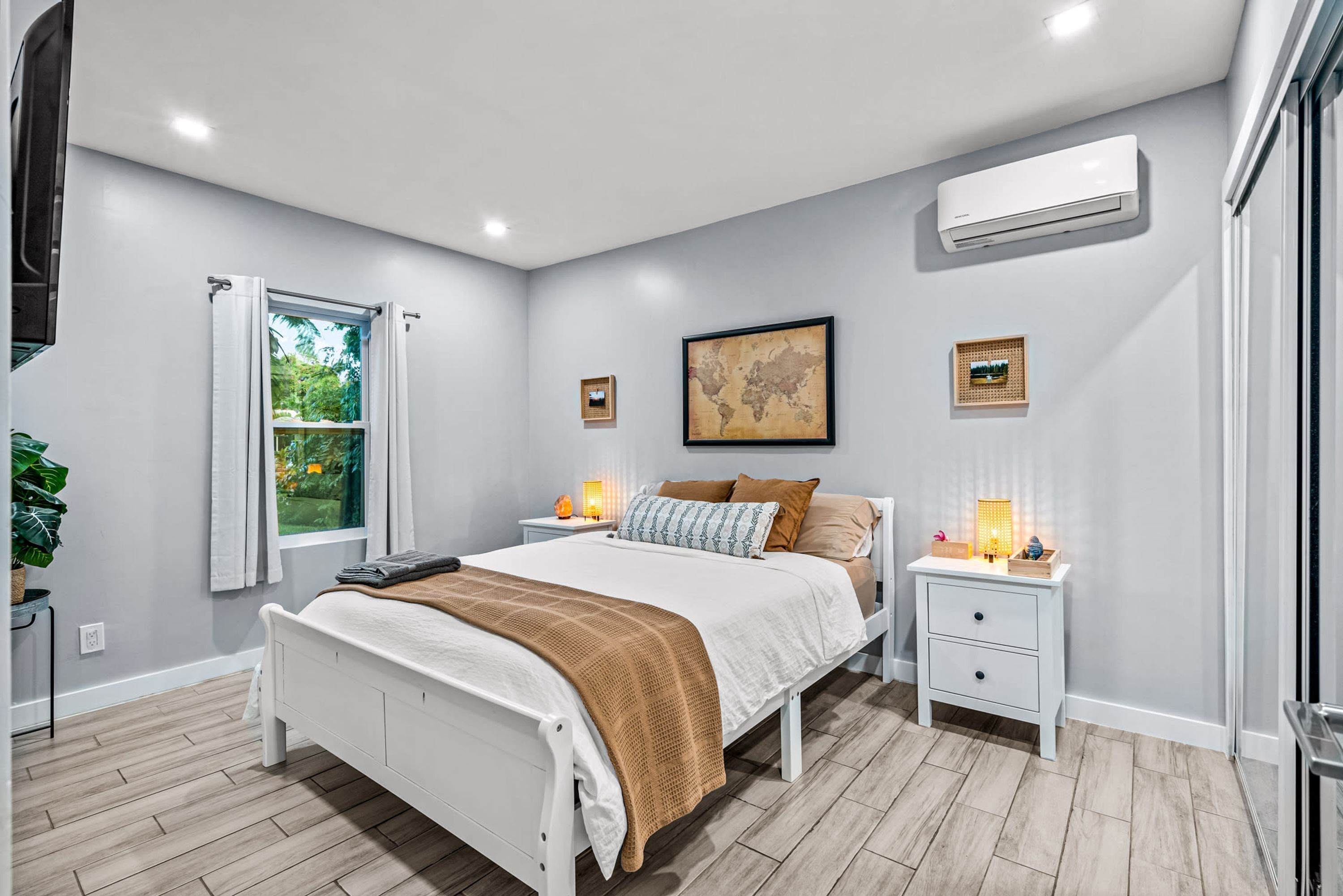 A modern bedroom with a bed, bedside tables, a window, and an air conditioning unit.