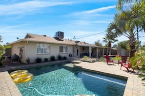 Une maison avec une piscine, du mobilier d’extérieur et des palmiers.