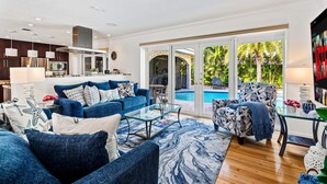 A spacious living room with a blue sofa set, a glass coffee table, and a patterned armchair. A pool is visible through the glass doors. - Cypress Cove - HTD Pool Near Lauderdale By The Sea (Fort Lauderdale)