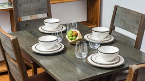 Une table à manger dressée avec des bols, des assiettes et des verres transparents, le tout entouré de chaises en bois.