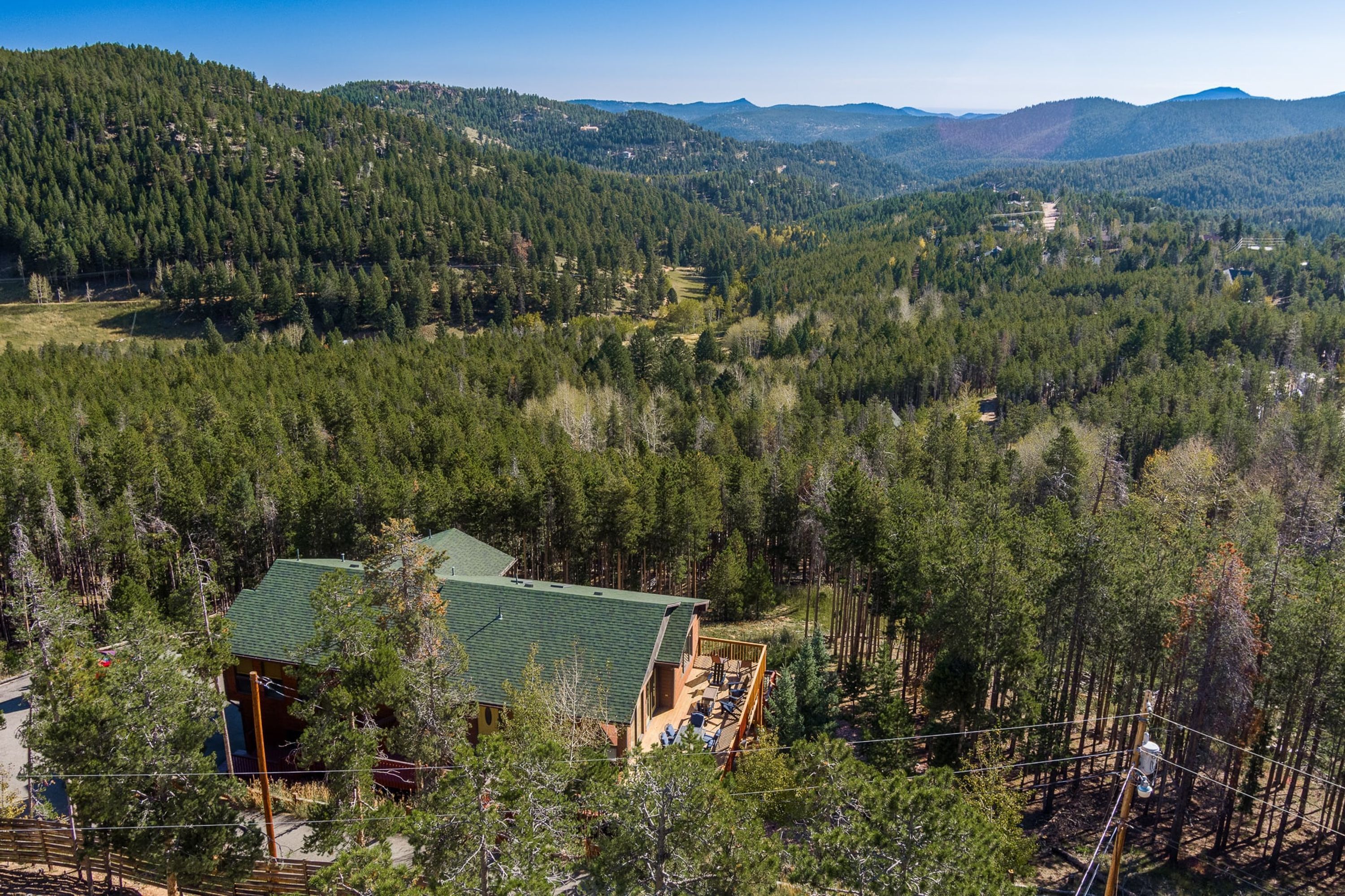 A lodge with a green roof, surrounded by dense forest and hills.