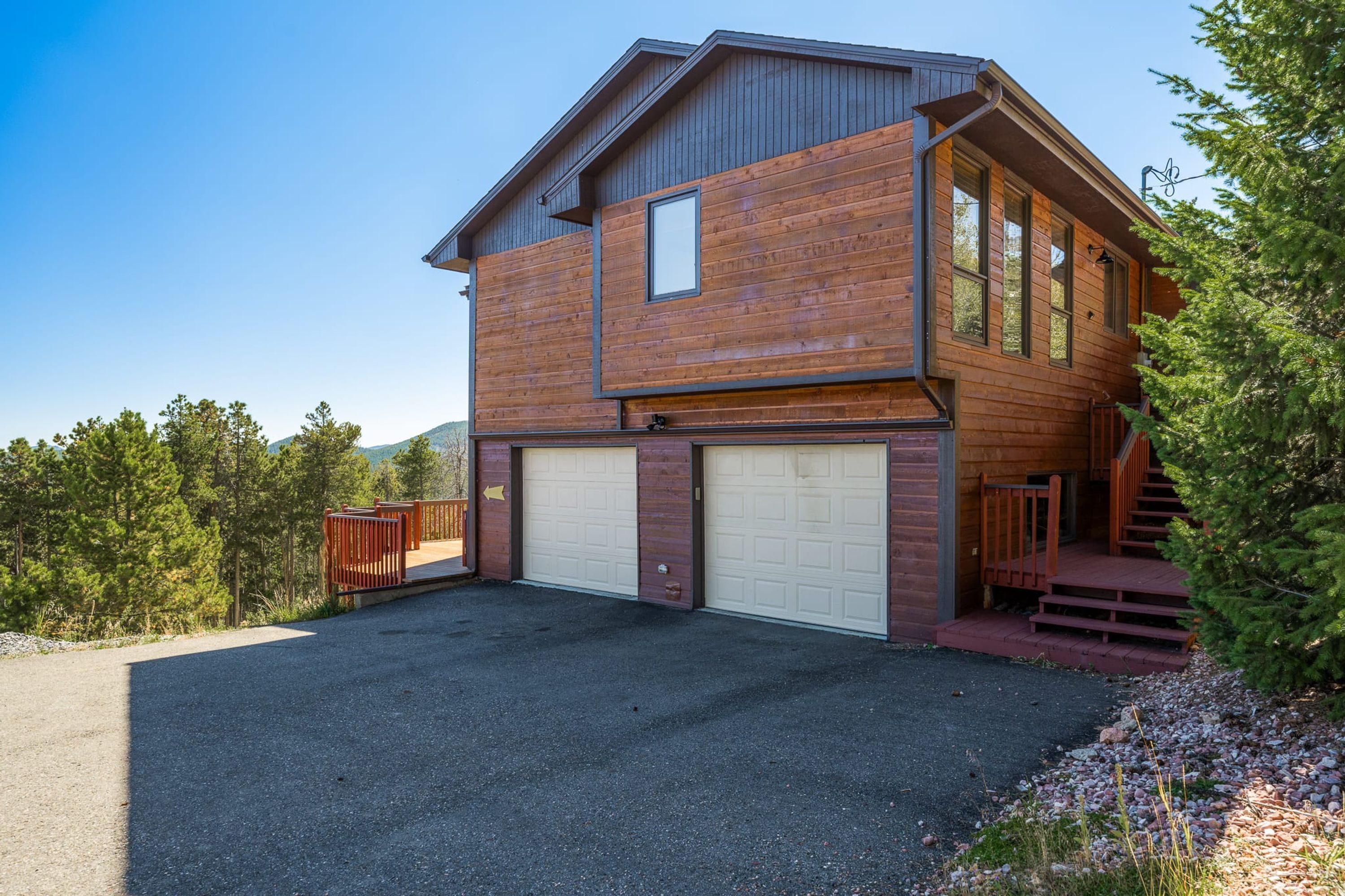 A two-story log cabin with a garage, a wooden deck, and a staircase leading to the main entrance.