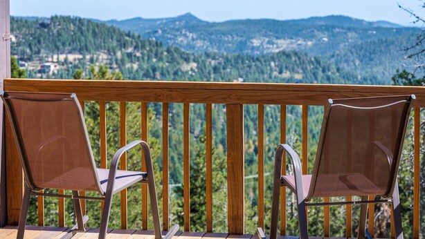 Un balcon avec deux chaises donnant sur un paysage pittoresque, avec une chaîne de montagnes boisées en toile de fond.