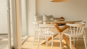 Un espace repas avec une table ronde, des chaises blanches et un luminaire suspendu en fibres tressées.
