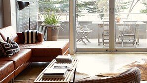 Un salon moderne avec un canapé en cuir, une table basse et une vue sur un balcon aménagé avec du mobilier d’extérieur.