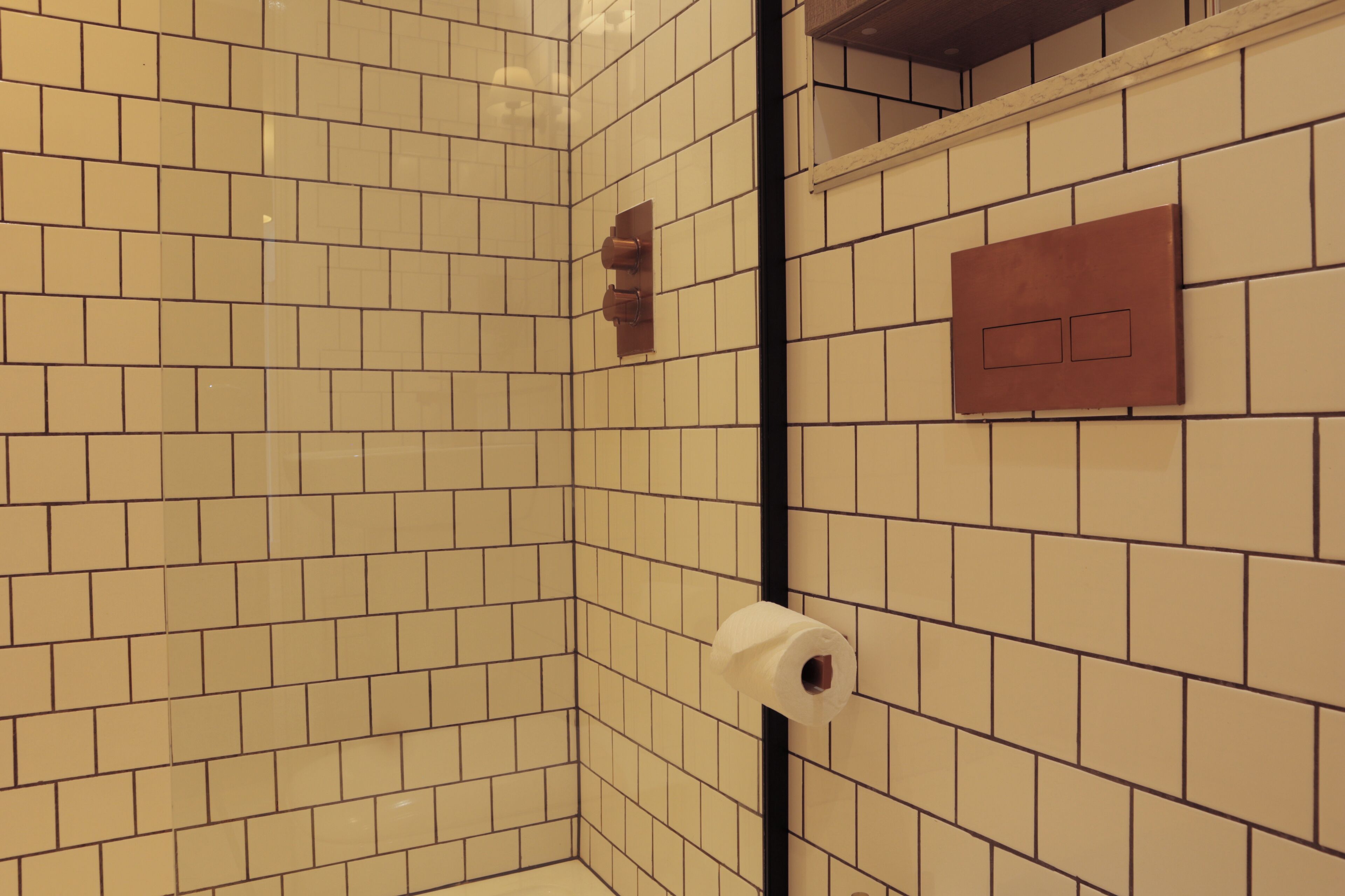 A bathroom with beige tiled walls, a toilet paper holder, and a flush handle.