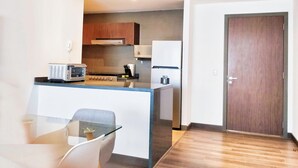 Une cuisine moderne équipée d’un four à micro-ondes, d’une cuisinière et d’un réfrigérateur. On aperçoit une table en verre avec une chaise au premier plan.