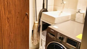 Une buanderie équipée d’un lave-linge, d’un évier et d’un support à serpillière.