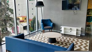 A modern living room with a blue sofa, a round coffee table, and a blue armchair. A TV is mounted on the wall, and there is a white TV stand with shelves. - Luxurious High-rise HS Wifi Amazing City Views (Mexico City)