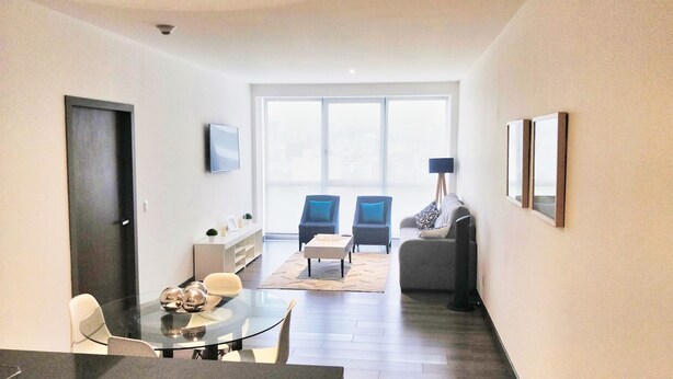 Een moderne woonkamer met een eethoek, een bank, twee fauteuils, een salontafel en een televisie aan de muur.