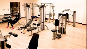 Een sportschool met diverse fitnessapparaten, een bank en een rek met dumbbells.