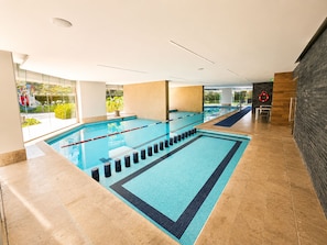 A swimming pool with clear lanes, a lifebuoy, and a view of greenery outside.