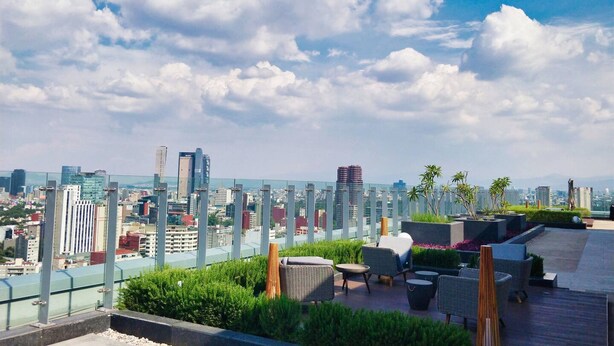 Terraza en la azotea con mobiliario exterior, vistas a la ciudad y barandilla de vidrio.