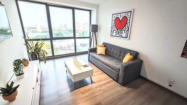 A modern living room with a grey sofa, a white coffee table, and a large window offering a city view. - Stunning Hi-rise Pool-jacuzzi gym HS Wi-fi (Mexico City)
