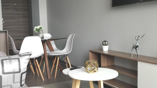 A modern living room with a sofa, two white chairs, a coffee table, a TV mounted on the wall, and a small shelf with decorative items. - Alluring Views Luxuriously Appointed in Polanco (Mexico City)