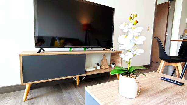 A modern living room with a flat-screen TV on a wooden stand, a small Buddha statue, and a potted orchid on a coffee table. - City View Oasis KS Bed Pool Hot Tub Gym (Mexico City)