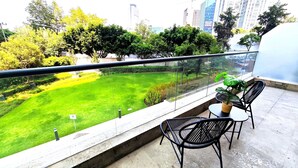 A balcony with a view of a well-maintained lawn and trees, a table with chairs, and a potted plant. - City View Oasis KS Bed Pool Hot Tub Gym (Mexico City)
