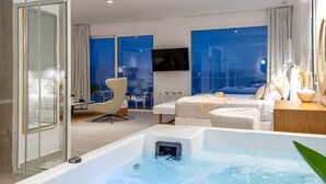 A modern hotel room with a large window, a bathtub, a bed, a chair, and a small table with a vase. - Achillion Luxury Corfu Villa (Corfu)