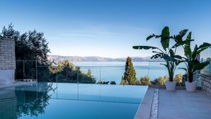 A swimming pool with a clear view of the mountains and a body of water. - Achillion Luxury Corfu Villa (Corfu)