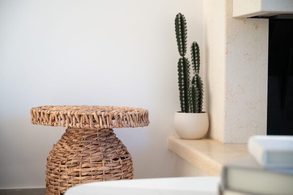 Un tavolino in vimini con un piano rotondo, un cactus in vaso e una parete bianca.