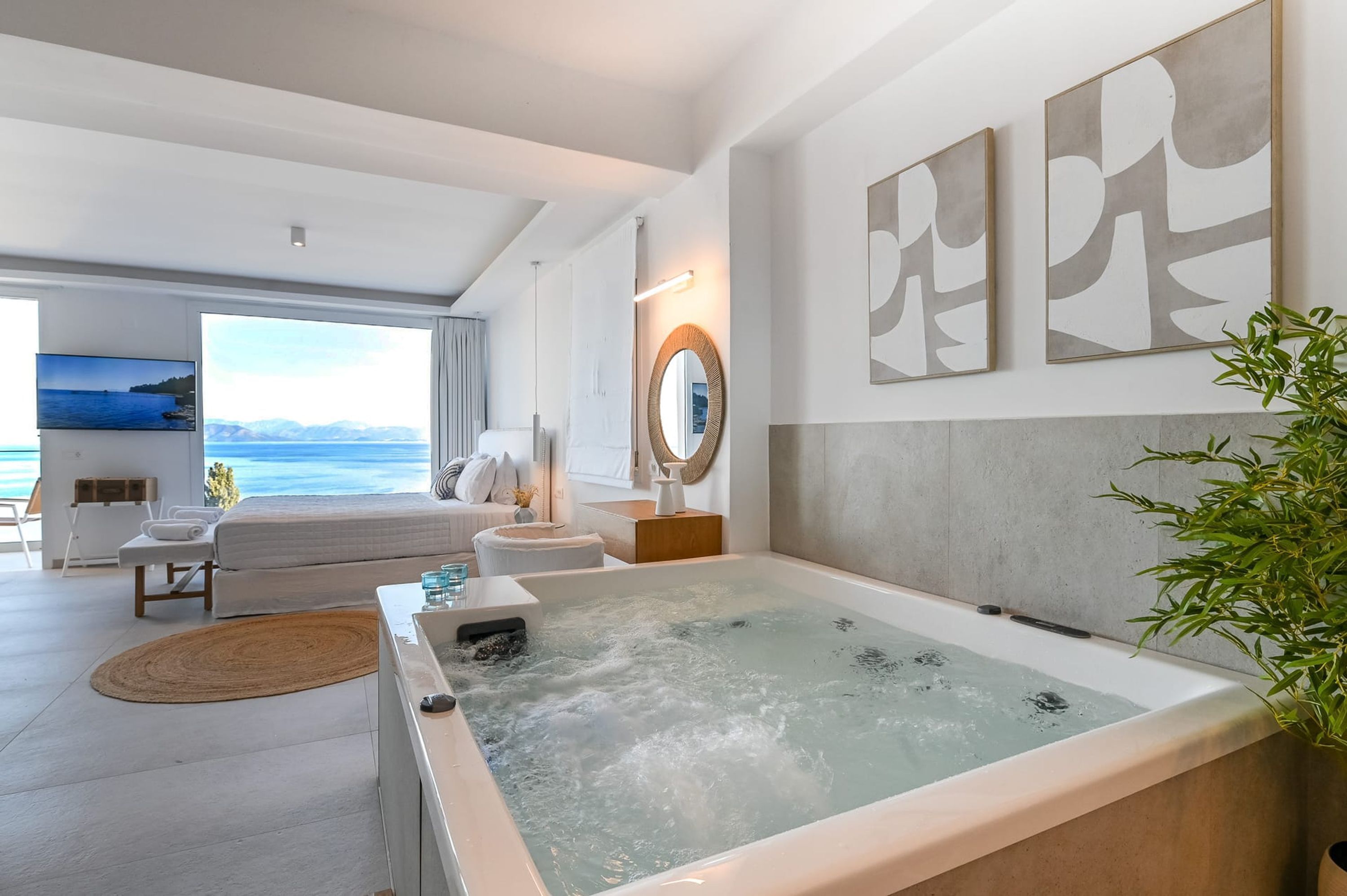 Ein modernes Hotelzimmer mit einer großen Badewanne, einer Couch, einem Fernseher und Blick aufs Meer.