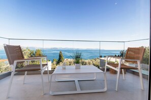 A balcony with two wicker chairs and a small table, overlooking a scenic view of the sea and distant mountains. - Achillion Luxury Corfu Villa (Corfu)