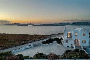 Une propriété située sur la côte, offrant une vue sur la mer, avec un bâtiment blanc doté de balcons et une allée pavée.