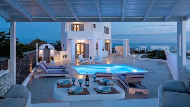 Un espace piscine extérieur moderne, doté de chaises longues, d’un coin repas et offrant une vue sur la mer.