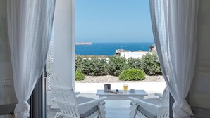 Une pièce avec vue sur la mer, une table avec un verre et deux chaises blanches.