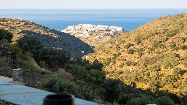 Una vista panorámica de una zona costera con una mesa y sillas, con vistas a una colina con edificios y al mar.