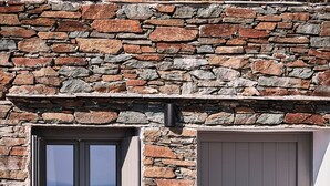 Un edificio de piedra con un gran ventanal y una puerta, un cartel que dice "Ado Alloni" y un felpudo con la leyenda "Villa L'Isola Residence".