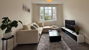 A modern living room with a sofa, a coffee table, a TV, and a large window. - 2 Bed Apartment - Sleeps 4, Balcony, Pets Ok (London)