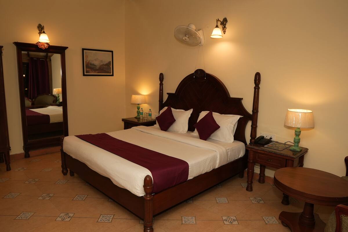 A neatly made bed with a wooden headboard, a bedside table with a lamp, a mirror, and a framed picture on the wall.