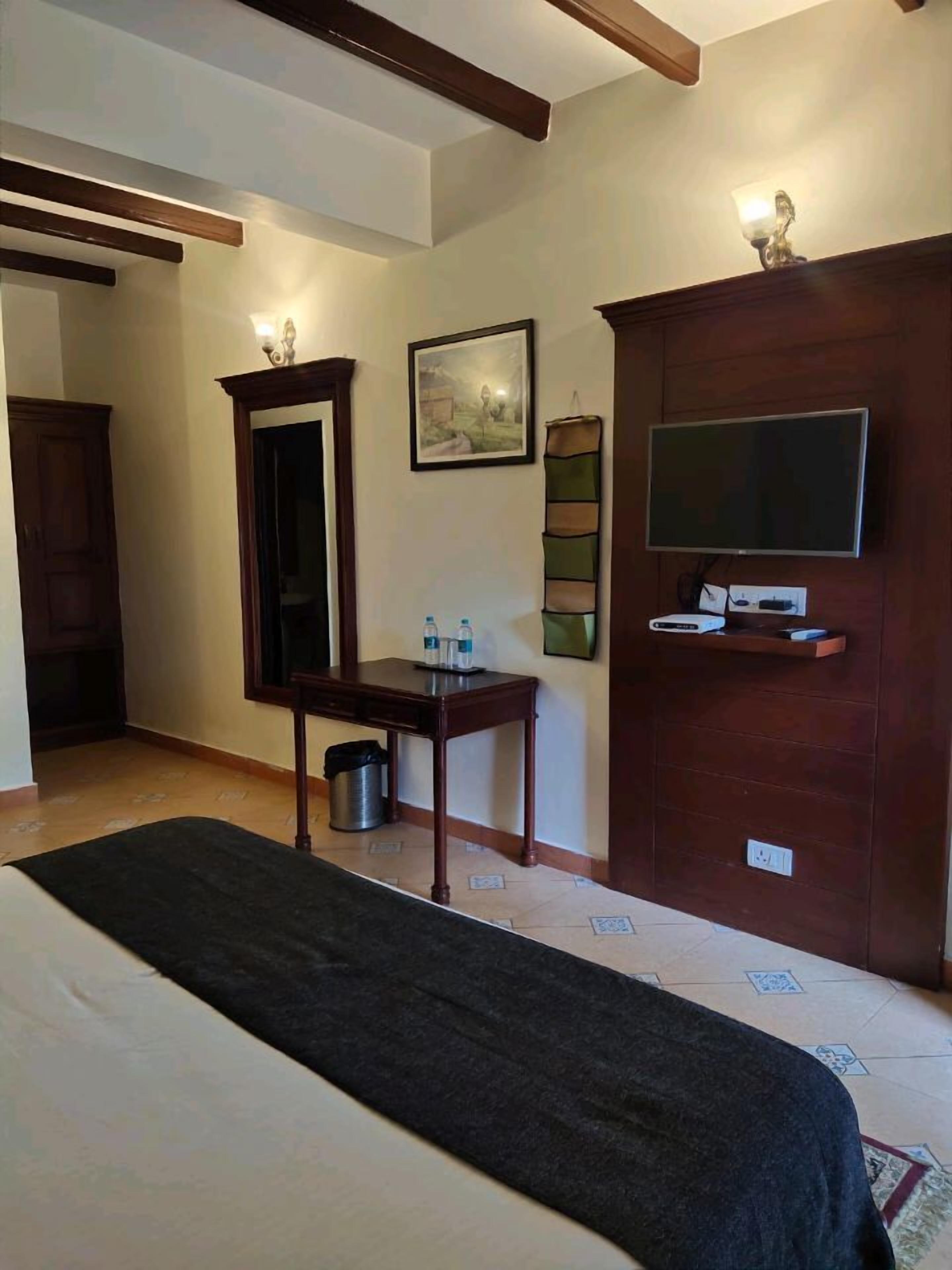 A hotel room with a bed, a desk with a mirror, a television on a wooden cabinet, and a painting on the wall.