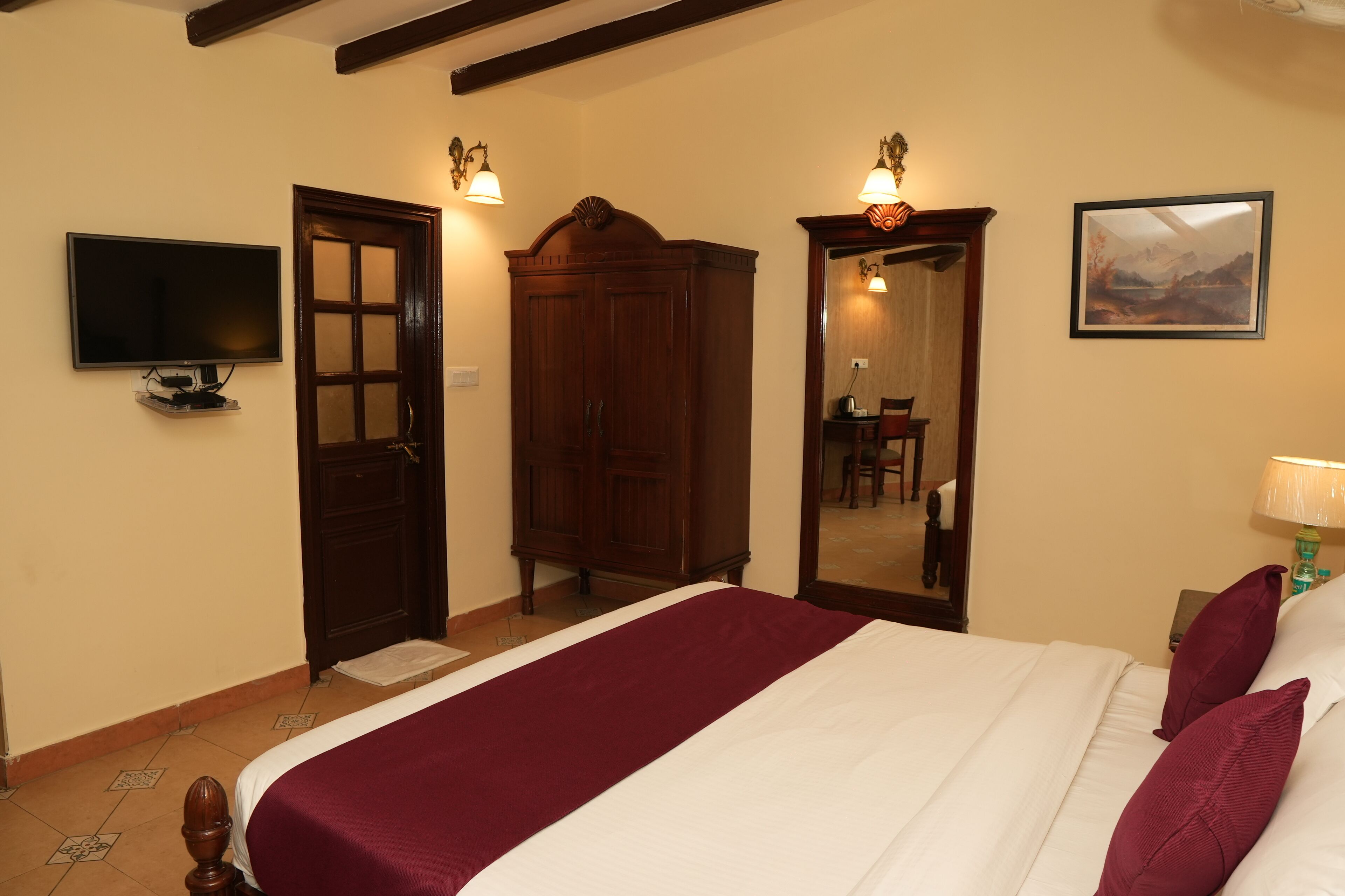 A bedroom with a large bed, a wardrobe, a television, and a mirror.