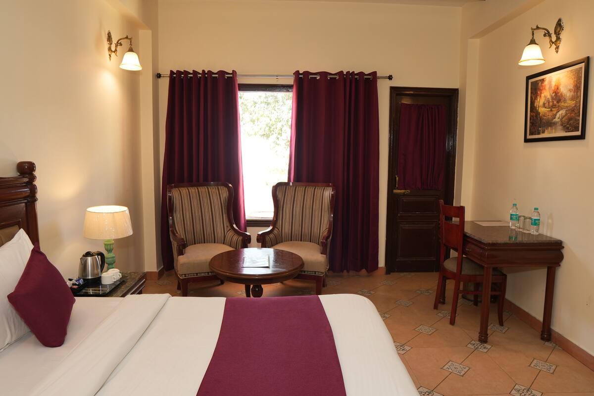 A hotel room with a bed, two armchairs, a small table, a desk, and a window with curtains.