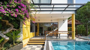 Un área de piscina moderna con suelo a cuadros, una entrada de cristal y una escalera que lleva a una zona cubierta.
