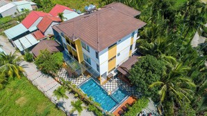 Un edificio de varios pisos con piscina, rodeado de exuberante vegetación y palmeras.