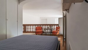 Un dormitorio con cama, dos sillones, una mesita y un balcón con barandilla.