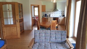 Une pièce chaleureuse avec un plancher en bois, un canapé bleu, une table à manger avec des chaises et un coin cuisine équipé de placards et d’une cuisinière.