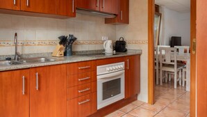 A compact kitchen with wooden cabinets, a stainless steel sink, a built-in oven, and a coffee maker. - Apartament amb Espectaculars Vistes al Mediterrani (Palafrugell)